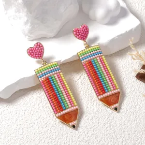 Creative beaded pencil earrings with a pink heart stud shown on a stone display
