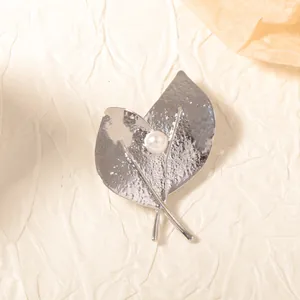Broche élégante en feuilles argentées texturées avec perle sur fond papier beige