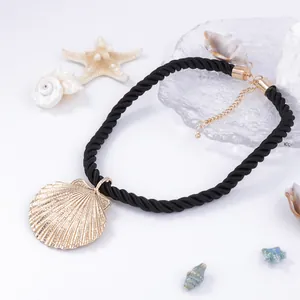 Detail of nautical gold shell pendant with black twisted cord on white background