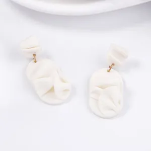 Detail showing white geometric petal earrings with textured fabric-like resin surface