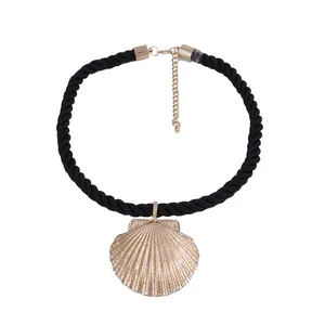 Detailed close-up of woven black cord necklace with a large golden scallop shell pendant