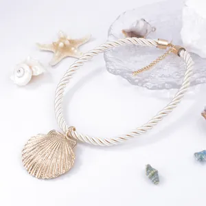 Detail of a golden scallop shell pendant on a cream braided rope beach necklace