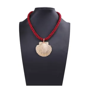 Close-up of golden shell pendant with red woven cord on black necklace display stand