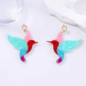 Détail des boucles d'oreilles colibri avec paillettes multicolores et perles blanches