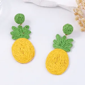 Handgemaakte raffia ananas oorbellen met felgeel geweven fruit en groene bladeren als accent