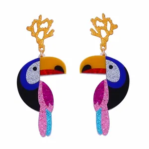 Détail de boucles d'oreilles toucan en résine acrylique scintillante et tiges dorées