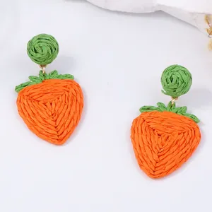 Handgeweven raffia aardbeien oorbellen met oranje textuur en groene bladeren op wit vlak