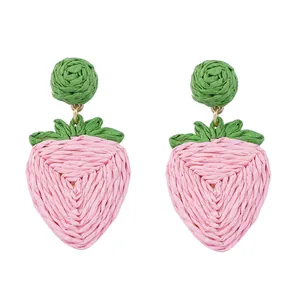Detail van handgemaakte aardbei oorbellen van geweven roze en groene raffia vezel