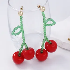 Detail view of handmade beaded cherry drop earrings with vibrant red spheres and green beads