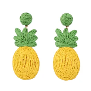 Detailopname van handgemaakte raffia ananas oorbellen met geweven gele en groene textuur