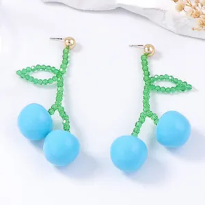 Beaded cherry earrings with light blue fruit and green leaf pendant on white background