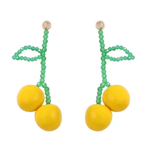 Detailed close-up of handmade cherry drop earrings with yellow beads and green glass leaves