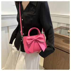 Detail of rose pink handbag with oversized bow decoration and shoulder strap on model