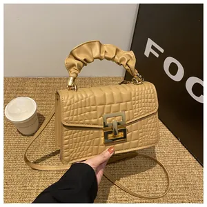 Detail of khaki crocodile embossed handbag with pleated handle and gold square buckle