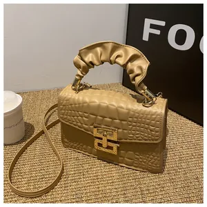 Detail of beige crocodile pattern leather handbag featuring a unique ruched top handle