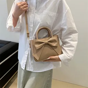 Minimalist light brown handbag with a large bow decoration and adjustable shoulder strap