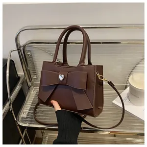 Detail einer braunen Handtasche mit großer Schleife und Herz-Strassstein in der Mitte