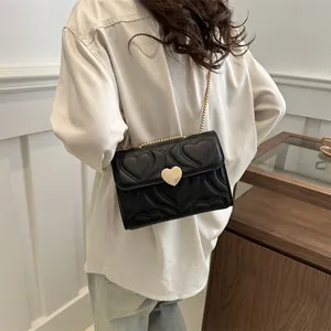 Elegant black heart-quilted chain shoulder bag with golden heart buckle on female model