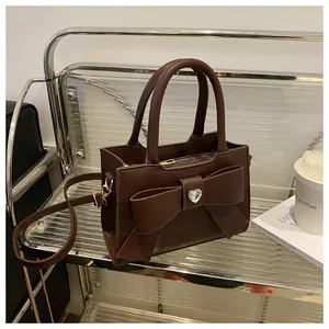 Detail einer dunkelbraunen Handtasche mit großer Schleife und Kristallherz auf Regal
