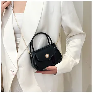 Detail of a black glossy mini bag with gold hardware and pearl on white blazer