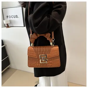 Detail of a brown crocodile pattern crossbody bag with a ruched handle and gold lock