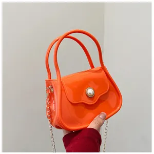 Detail of a shiny orange jelly handbag with a large pearl clasp and gold chain strap