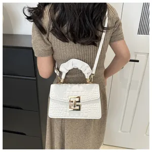 Detail of white crocodile pattern crossbody bag with ruffled handle and golden lock
