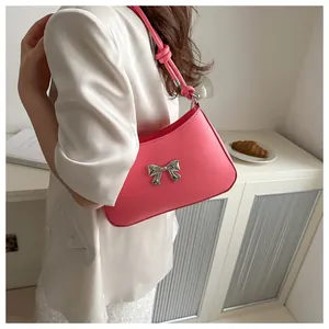 Pink underarm bag with silver metal bow and knotted handle worn by a model