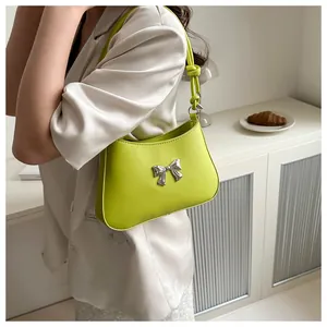 Detailed close-up of light green shoulder bag featuring a silver metal bow and knotted strap