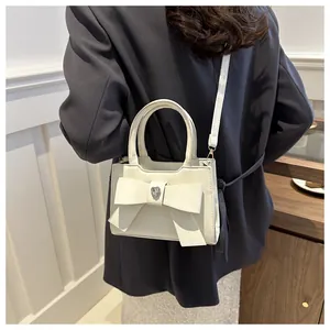Detail der cremeweißen Leder-Umhängetasche mit Schleife und herzförmigem Diamantakzent