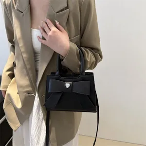 Schicke schwarze Umhängetasche mit Schleife und Herz-Strassstein am beige Blazer-Model