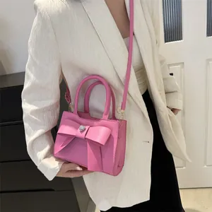 Rosa Umhängetasche mit großer Schleife und Herz-Strassstein auf weißem Blazer gezeigt