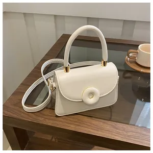 Detail of white PU leather small square bag with gold hardware and top handle on table