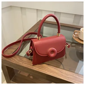 Detail of burgundy square handbag featuring a round decorative buckle and gold hardware