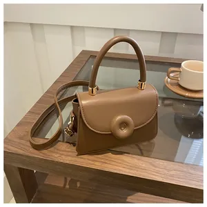 Detail of a brown leather crossbody bag with round buckle on a wooden cafe table