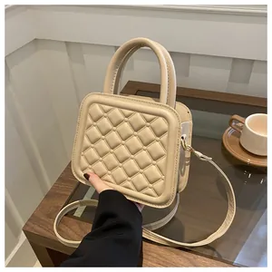 Detail of beige quilted mini square bag with leather handle on a stylish glass table