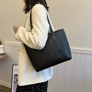 Large black tote bag with embossed wavy texture shown on a shoulder in a stylish home setting