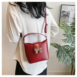 Model showing a stylish red bucket bag with a golden bow buckle in a minimalist setting