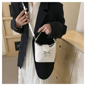 Close-up of white crossbody bucket bag with silver metal bow and adjustable strap