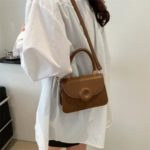 Minimalist caramel brown leather handbag with round buckle and golden hardware