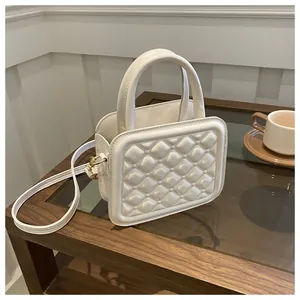 Detail of cream quilted crossbody bag with textured 3D square pattern and gold hardware