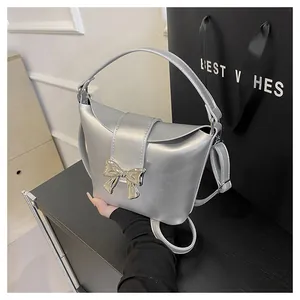 Close-up of silver metallic bucket bag featuring a golden bow buckle and fine texture