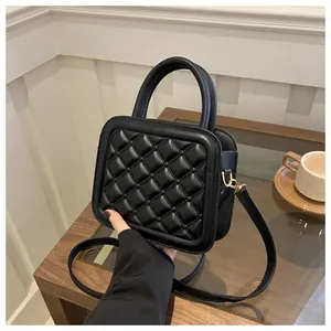 Detail of black quilted crossbody bag with golden hardware on a wooden table