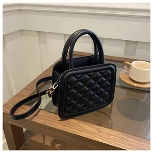 Detail view of a black quilted leather mini bag on a wooden table with a gold metal clasp