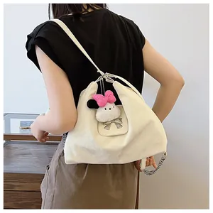 Detail of cream hobo bag with silver chain strap and plush cartoon pendant on shoulder