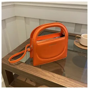 Detail of bright orange leather handbag with integrated semicircular handle and silver zipper