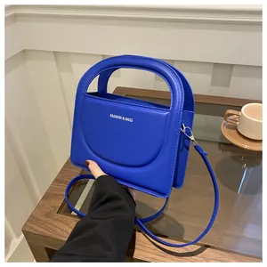 Blue leather handbag with cutout handle and white text detail held in a lifestyle setting