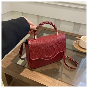 Macro view of burgundy crocodile pattern handbag showing glossy texture and gold buckle