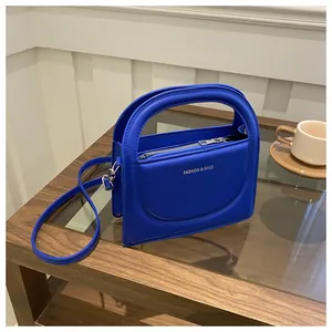 Close-up of vibrant blue faux leather crossbody bag with silver zipper and curved handle