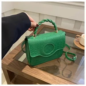 Detail of green faux leather handbag with crocodile pattern and braided handle